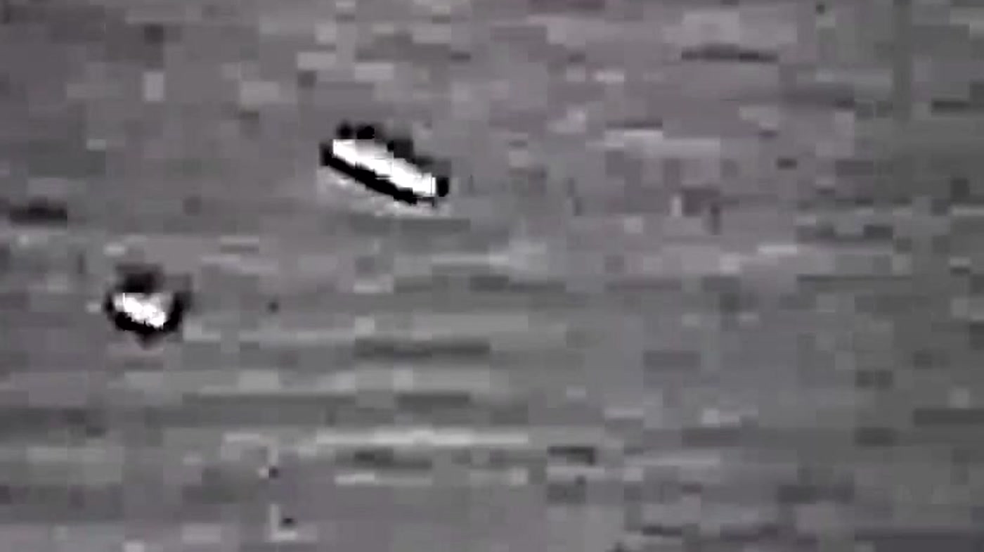 The two objects from the hero frame, cropped and enlarged with a modest contrast lift. The upper object is elongated with a bright upper surface and a dark underside, the lower one is smaller and rounder. No scale, altitude or range can be derived, because the sensor readout is the part the Department redacted.