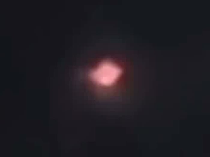 A brightened crop of the released National Archives footage, showing the soft glowing form the officers described as cycling through colors. The smearing into a rounded shape is consistent with a bright point filmed through binoculars on a phone.