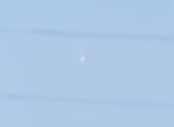 A zoomed crop of the reported object. It reads as a small soft pale light against the twilight sky, between two power lines and with no resolvable structure.