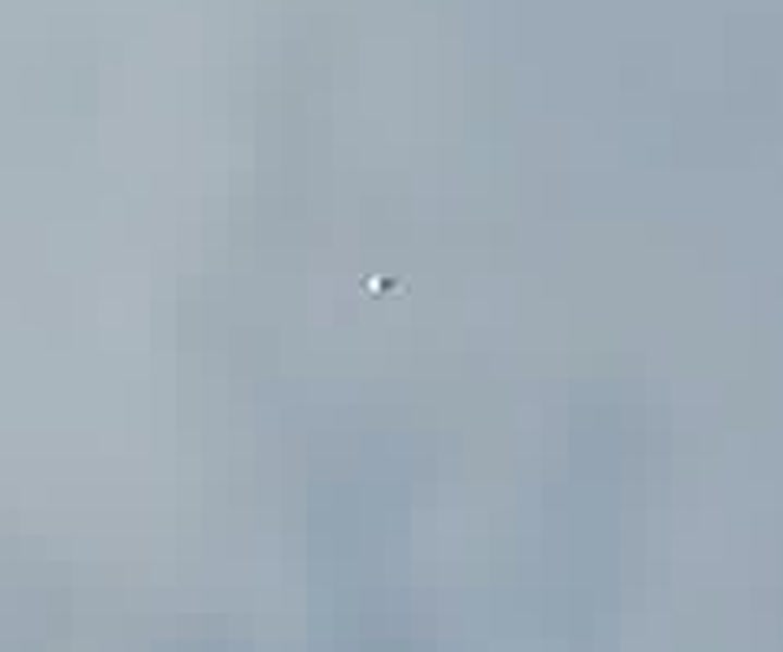 A zoomed crop of the object from the same frame, enlarged. The bright, slightly elongated form is consistent with a reflective sphere blurred by its speed.