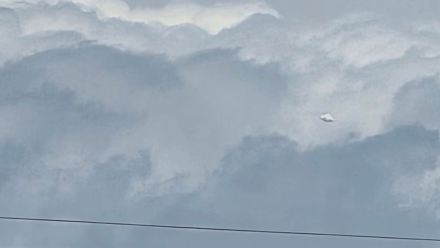 A second frame from the same short sequence, the object still holding its smooth lozenge shape against the dark cloud. Witness photograph.