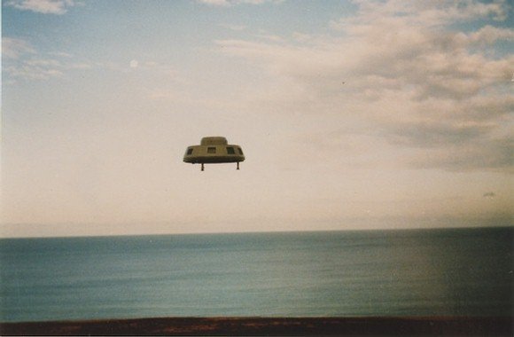 First frame: the disc low over the sea off Ochre Point with three landing legs still extended, moments after Thomason says it rose from the water.