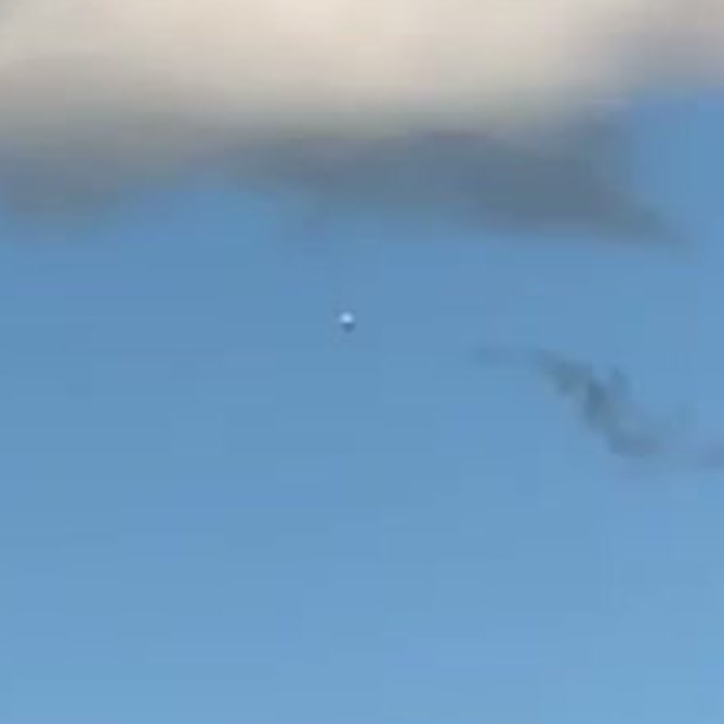 A zoomed crop of the object. It reads as a small pale sphere against the blue sky, with no resolvable structure.