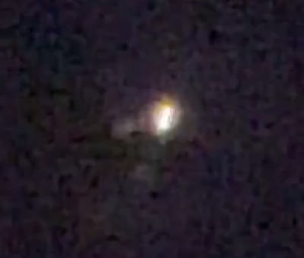 A zoomed crop of the light. It reads as a brilliant warm core with a secondary point or streak to one side, the kind of profile a reflection or a distant aircraft light can both produce.