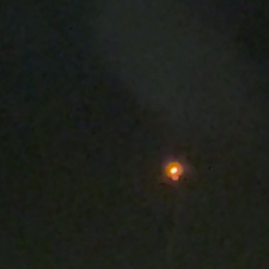 Native-resolution crop of a single object from the witness video, about 42 seconds in. The rounded glowing envelope sits above a thinner luminous trail that resolves into discrete bright specks. Across the sequence that trail stays pointed downward while the object drifts, which is the behaviour of something hanging under gravity rather than an optical smear following the direction of travel. Frame extracted by UAP Globe from the witness footage.