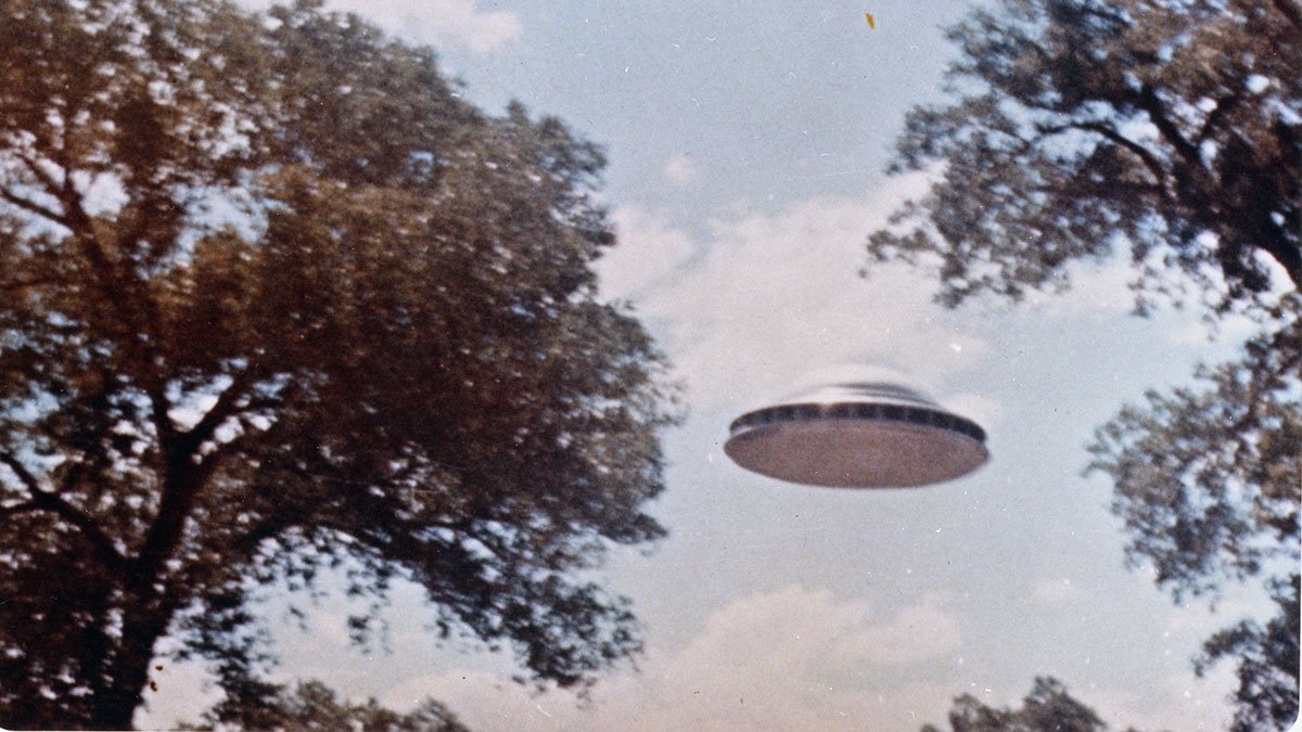 The best-known Paul Villa photograph: the silver domed saucer with a dark porthole band between two cottonwoods along the Rio Grande bosque. This print is held by the US National Archives as Flying Saucer, June 4, 1964 (local ID 255-GS-65-108, NASA Goddard graphics collection, RG 255); the contactee literature dates the tree-framed series to 16 June 1963, a discrepancy the archives themselves carry.