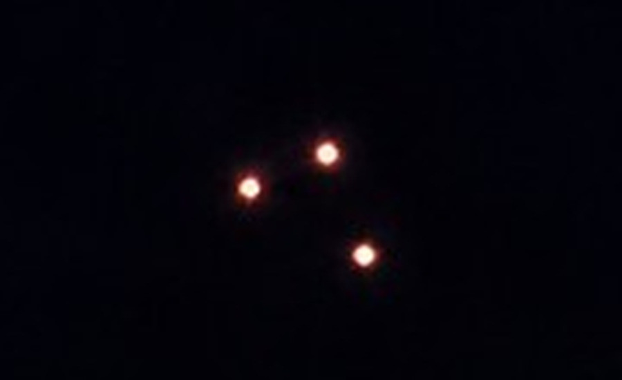 The three objects cropped and enlarged five times from the same published frame. They are soft round amber point sources with no edge, no silhouette and no light of any kind in the space between them, and the spacing of the triangle is uneven rather than fixed. This is what the case turns on: the witness reported the arrangement held, and also reported that no structure was visible, and the frame agrees with both halves of that statement.