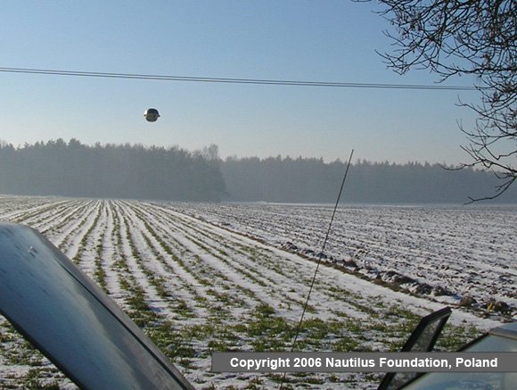 The sphere low over the furrowed snow field, with the witnesses' Polonez hood in frame. Nautilus stressed the unbroken snow shows no footprints from any thrower.